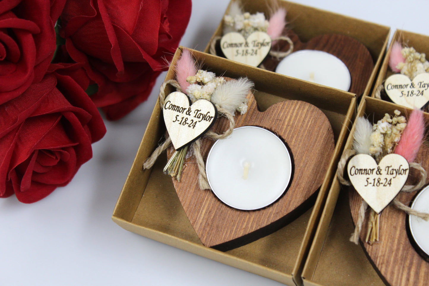 Personalized heart-shaped wooden candle holder featuring dried floral accents, perfect for romantic wedding favors. Each holder includes a tea light and a customizable wooden heart tag with the example names 'Connor & Taylor' and date '5-18-24.' Ideal for adding a touch of rustic elegance to wedding celebrations, these handcrafted wooden candle holders come beautifully presented in a box, with red roses enhancing the romantic appeal.