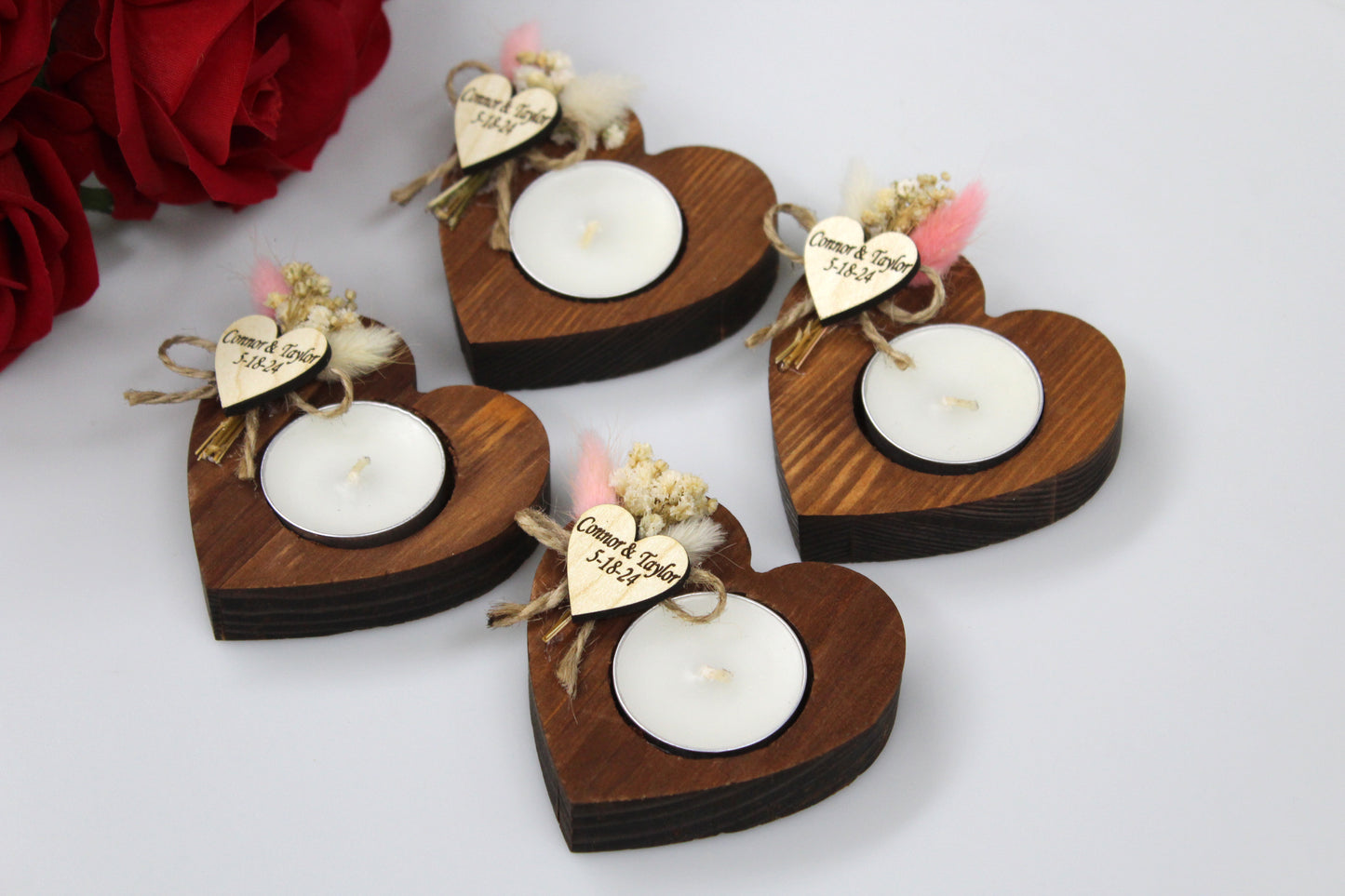 Exquisite Personalized Heart-Shaped Wooden Candle Holders with Dried Flowers. Each holder features a rustic wooden heart design, a white tealight candle, and a personalized wooden heart tag with dried flower accents. Ideal for wedding favors, adding a touch of natural elegance and customization to your special day. Example names and dates shown for personalization.