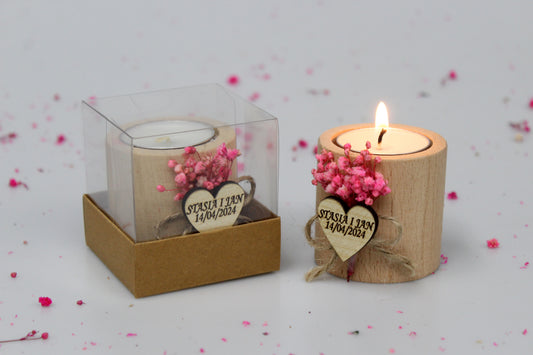 Personalized wooden tea light candle holders adorned with pink dried flowers, perfect for wedding favors. One candle holder is lit, while the other is packaged in a clear box. Example names 'Stasia I Jan' and date '14/04/2024' are shown on the heart-shaped tags, highlighting customization options