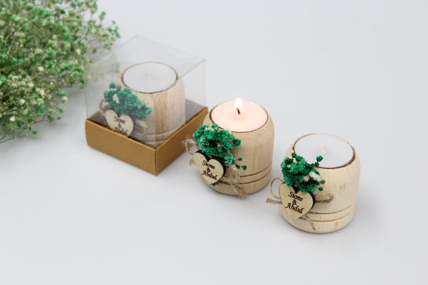 Charming wedding display featuring personalized wooden candle holders adorned with delicate green floral accents. Perfect for adding a touch of rustic elegance to any celebration. Names and dates are just examples for users.