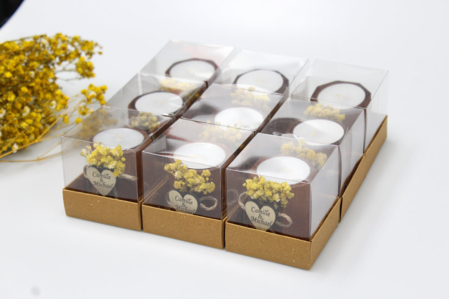 Set of elegant personalized wooden candle holders with yellow dried flowers, perfect for wedding favors. Each handcrafted piece features a heart-shaped tag engraved with example names 'Camille & Michael,' beautifully packaged in a transparent gift box. These rustic candle holders add a romantic touch to any celebration, ideal for enhancing wedding decor