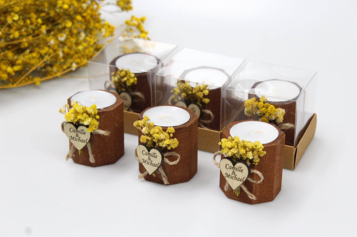 Personalized heart-shaped wooden candle holders adorned with dried flowers, featuring custom engraved tags. These rustic wedding favors are elegantly packaged, showcasing a charming and natural design. Ideal for adding a touch of personalized beauty to wedding decor and gifts.