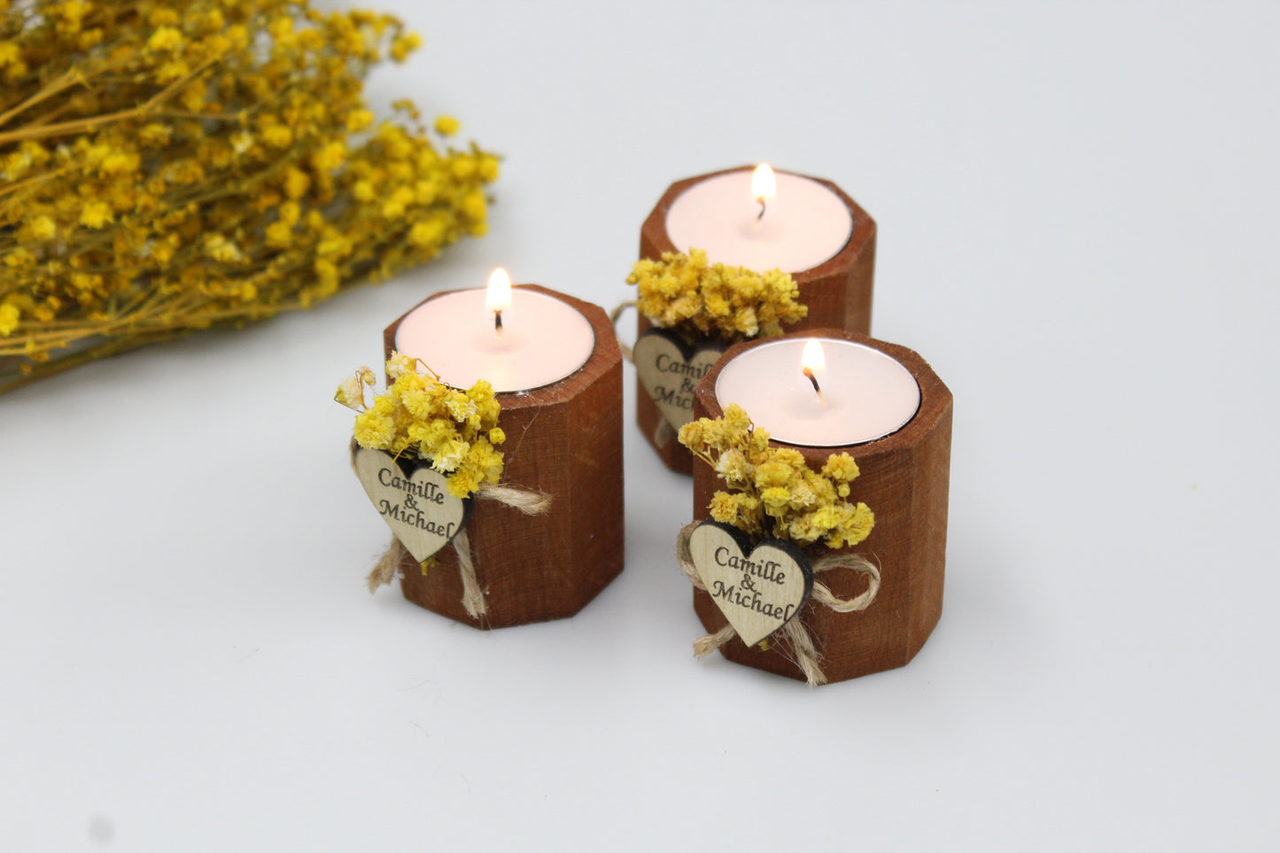 Enchanting trio of personalized wooden candle holders adorned with delicate dried flowers and custom engraved heart tags, featuring the names Camille & Michael. These handcrafted wedding favors, glowing with elegance and rustic charm, are perfect for creating an unforgettable ambiance. Ideal for sophisticated wedding decor, each piece exudes bespoke craftsmanship, making them the ultimate keepsake for your special day.