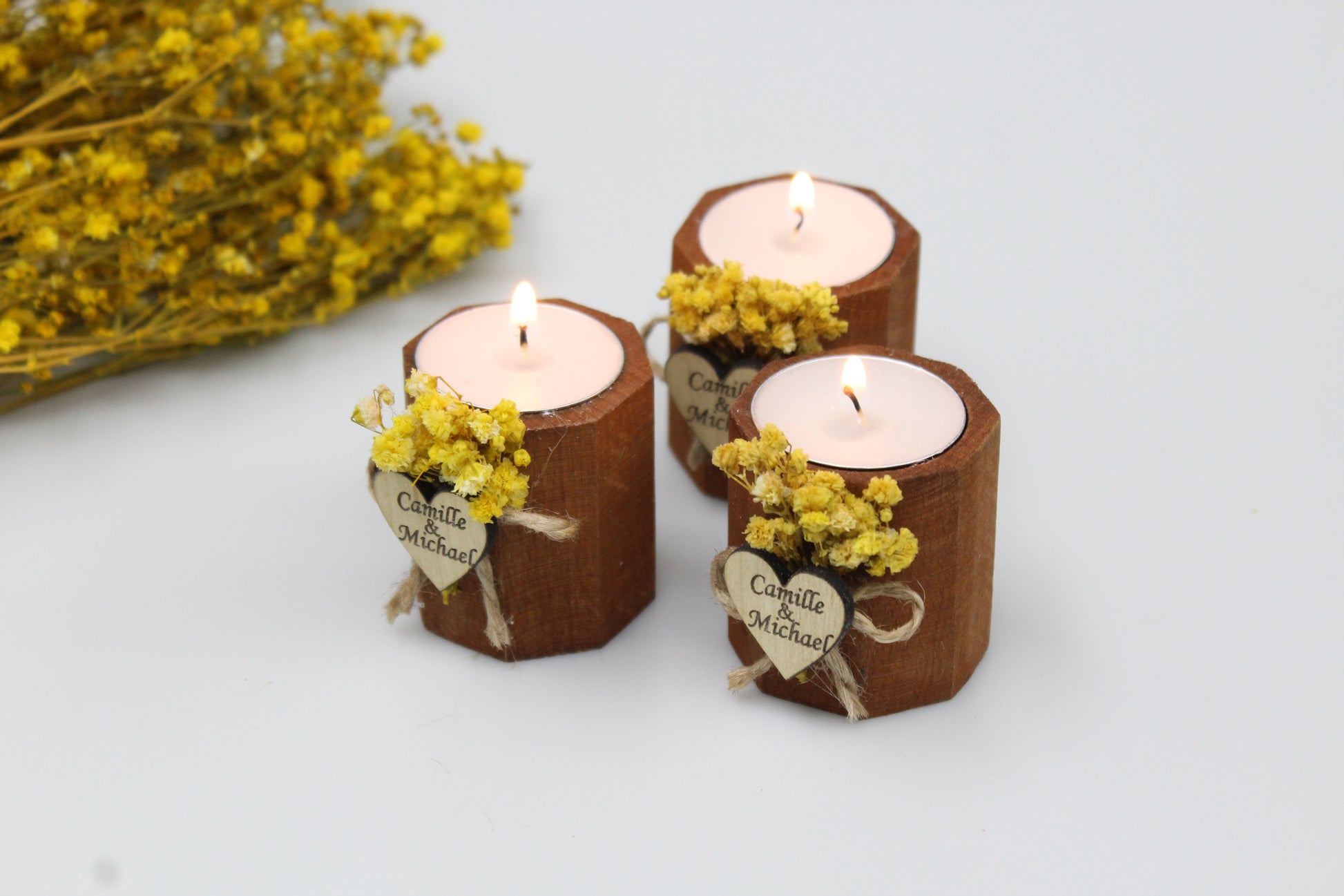 Enchanting trio of personalized wooden candle holders adorned with delicate dried flowers and custom engraved heart tags, featuring the names Camille & Michael. These handcrafted wedding favors, glowing with elegance and rustic charm, are perfect for creating an unforgettable ambiance. Ideal for sophisticated wedding decor, each piece exudes bespoke craftsmanship, making them the ultimate keepsake for your special day.