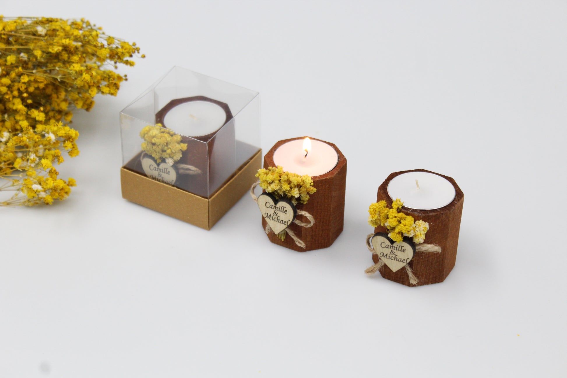 Exquisite display of personalized wooden candle holders featuring intricate dried floral arrangements and custom engraved heart tags with the names Camille & Michael. These handcrafted wedding favors, shown in various stages from boxed to lit, exude rustic elegance and charm, making them perfect for creating a warm, romantic atmosphere at your celebration. Ideal for sophisticated wedding decor, each piece showcases bespoke craftsmanship, ensuring your guests receive a memorable keepsake.