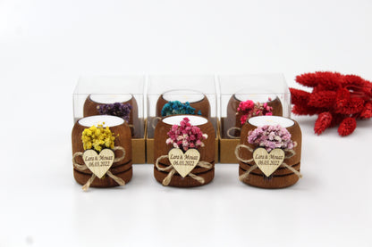 Handcrafted wooden tea light candle holders with colorful dried flower arrangements and personalized heart-shaped tags. Each holder is packaged in a clear box, making them perfect for rustic wedding favors. Example names and dates are displayed, showcasing their customizable features.