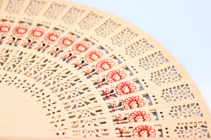 Close-up of a rustic wooden hand fan with detailed lace patterns and red floral designs, ideal for wedding favors.