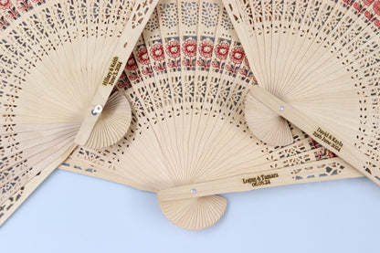 Collection of personalized rustic wooden hand fans with intricate lace patterns and red floral designs, engraved with wedding dates and names, ideal for wedding favors.