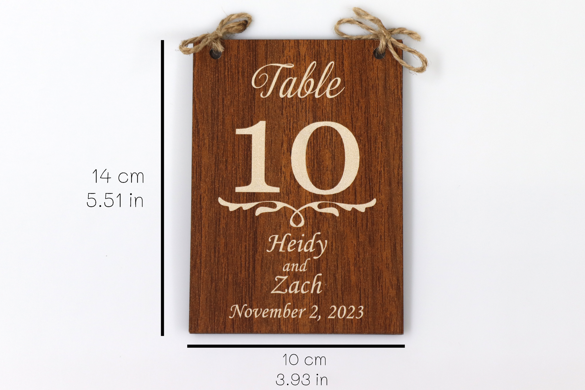 A personalized wooden table number sign for a wedding, displaying 'Table 10' with the names 'Heidy and Zach' and the date 'November 2, 2023.' The sign features a dark wood finish and includes dimensions: 14 cm (5.51 in) in height and 10 cm (3.93 in) in width.