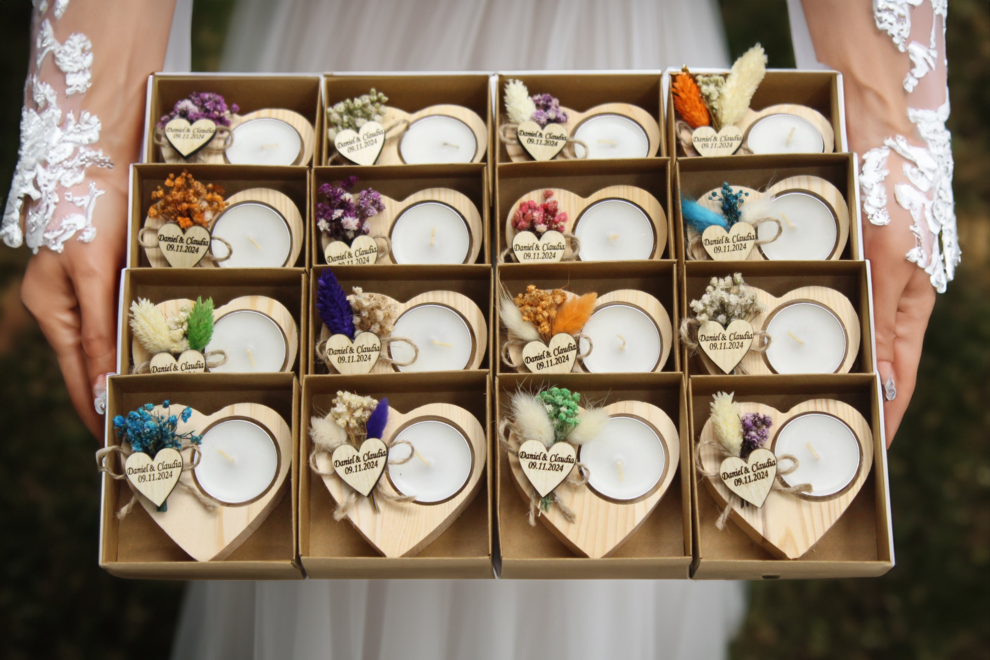 Elegant display of personalized heart-shaped wooden candle holders with dried flowers, custom engraved tags, and names and dates as examples. Held by a bride in a lace-sleeved gown, these rustic yet elegant wedding favors add a romantic touch to your celebration. Perfect for decor and keepsakes, each holder is meticulously crafted, creating a cherished memento for guests.